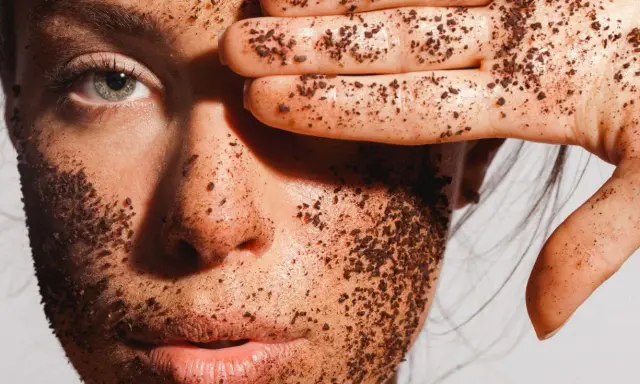 Visage couvert de grains d'un exfoliant chimique naturel, une main cache un œil.