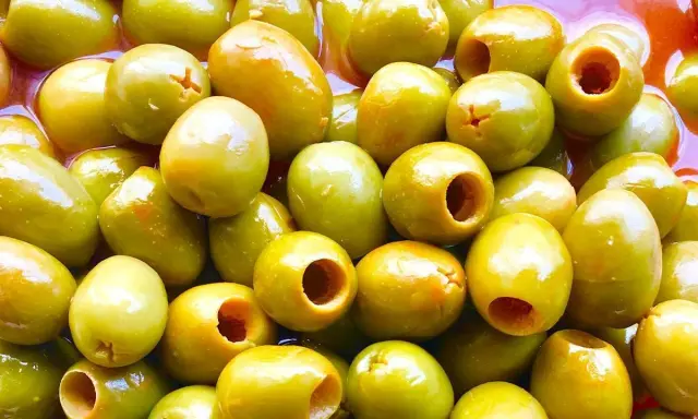 Un primer plano de muchas aceitunas verdes, algunas deshuesadas, listas para ser parte de las clases de aceitunas para comer.