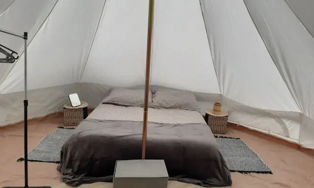 Komfortowy glamping nad morzem: łóżko z pościelą, stoliki nocne, wieszak i namiot.