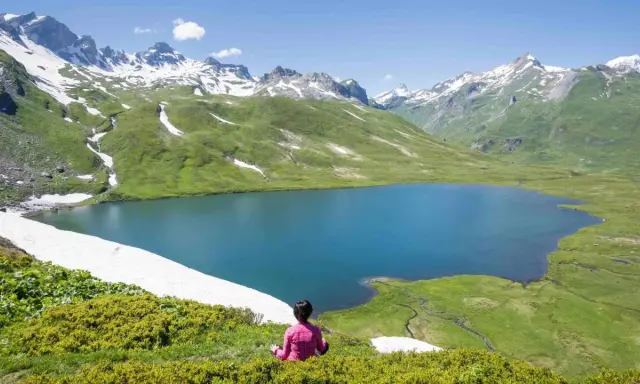 Pace e natura in Valle d'Aosta in estate: un lago alpino azzurro circondato da montagne innevate e verdi pascoli.