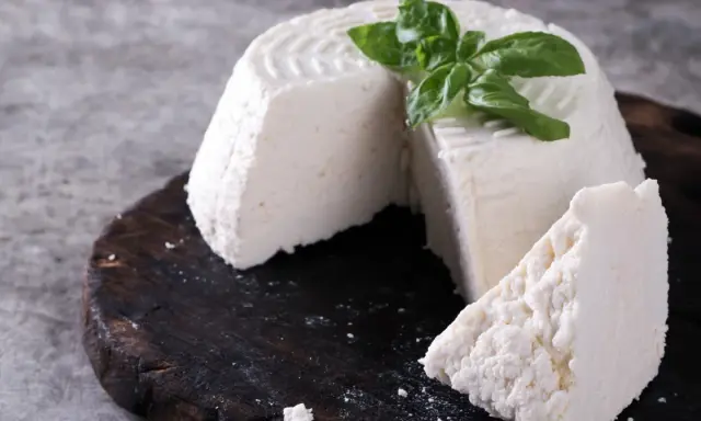 Świeża ricotta z bazylią na ciemnej desce.