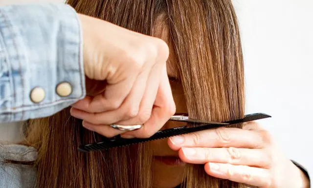 Eine Person schneidet sich mit Kamm und Schere die Haare, um Curtain Bangs zu kreieren.