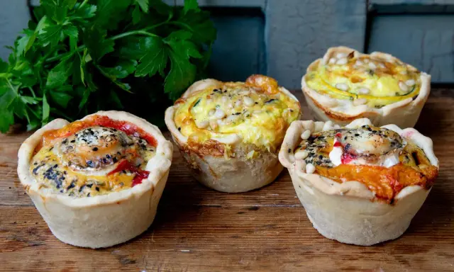 Vier köstliche Mini-Quiches mit verschiedenen Füllungen, perfekt für ein schnelles mini quiche rezept. Mit Petersilie garniert.