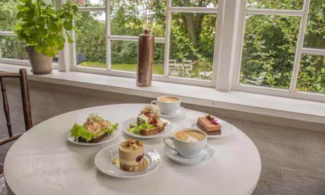 Fika på ett mysigt cafe i Skåne med smörgåsar, tårtor och kaffe.