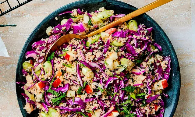 En färgglad couscous sallad med rödkål, äpple och mynta. En gyllene sked vilar i den fräscha rätten.