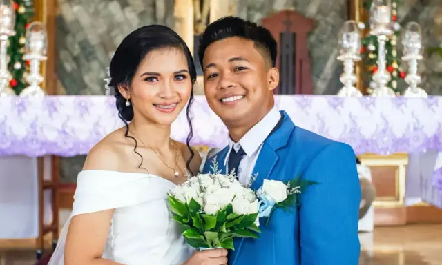 Novios sonriendo, ella con vestido blanco y él con traje azul. Un ramo de rosas blancas. Agradecimiento a los novios por la boda.