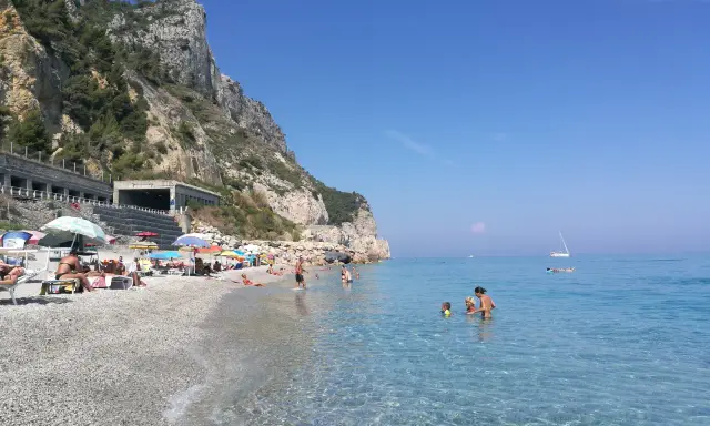 Varigotti spiaggia più bella: gente rilassata sotto gli ombrelloni, mare cristallino e scogliere imponenti.