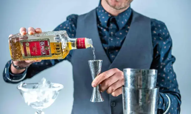 Barman nalewa Olmeca Tequila Gold do miarki, idealna tequila do margarity. Obok kieliszek z lodem i shaker.