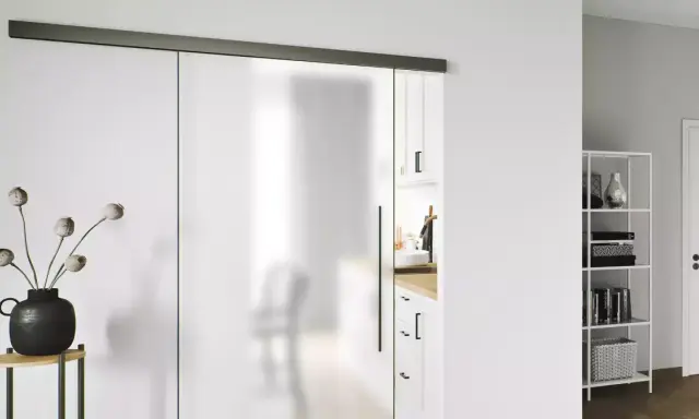 Puerta corredera de cristal esmerilado con tirador negro. Una guía superior negra y un riel inferior negro son clave para como poner una puerta así.