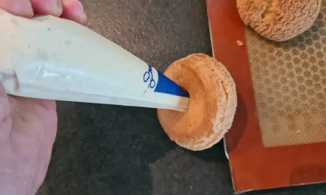Garnissage d'une pâte à choux profiterole avec une crème onctueuse à l'aide d'une poche à douille.