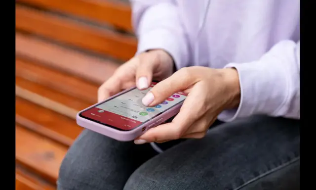 Dłonie kobiety obsługują smartfon, który wyświetla listę e-maili. To przykład interakcji, która może wykorzystywać haptykę – co to za technologia?