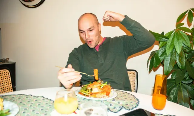Mann feiert sein **Essen nach Marathon** mit einem kräftigen Bizeps-Zeigen und einem Bissen vom Teller.