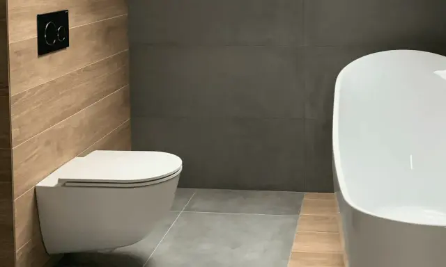 Salle de bain moderne avec un élégant **pose wc suspendu** sur un mur en bois, face à une baignoire blanche et des murs gris.