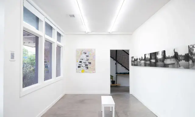 Inside the Atlanta Center for Photography, a white bench sits before a map artwork. Black and white photos line the opposite wall.