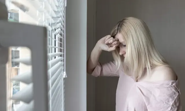 Mujer rubia con la mano en la frente, mirando hacia abajo, con un aire de melancolía que evoca el síndrome de Wendy.