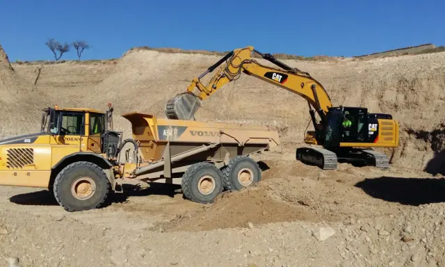 Excavadora CAT cargando volquete Volvo en obra de movimiento de tierras.