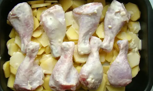 Osiem pałek kurczaka w sosie, ułożonych na plastrach ziemniaków w brytfannie. Idealne do pieczenia, by uzyskać chrupiące pałki z kurczaka w piekarniku.
