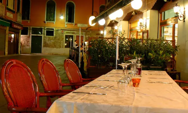 Table dressée devant la trattoria "da Roberto" à Venise, avec des chaises rouges et des verres à vin.