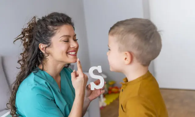 Logopeda pomaga dziecku z dyslalią ćwiczyć wymowę litery "S", używając białej literki.