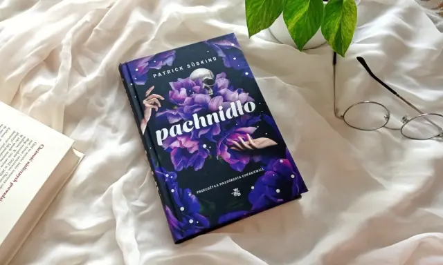 Powieść Patricka Süskinda "Pachnidło" na tle białej tkaniny, obok okularów i innej książki.