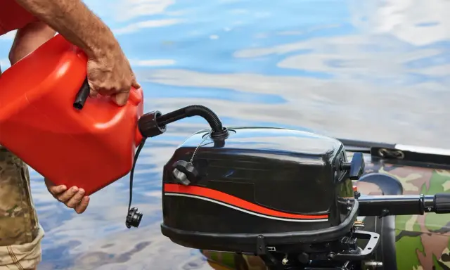 Un homme verse de l'essence dans un moteur hors-bord. Il se demande quel essence pour moteur 2 temps utiliser pour sa sortie en bateau.