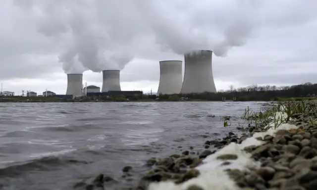 Kühltürme eines Atomkraftwerks mit Dampfschwaden über einem Flussufer.