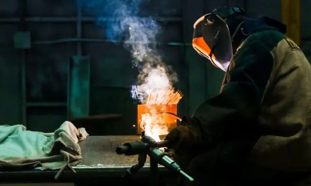 Soldador usa un electrodo rutilo para crear uniones fuertes. El humo y las chispas iluminan la escena industrial.