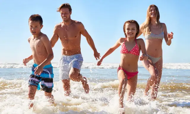 Famiglia corre felice nel mare del lido di Savio, spruzzi d'acqua e sole.