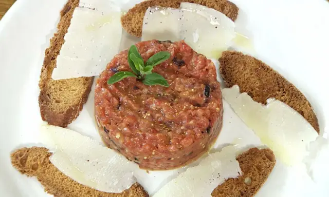Delicioso tartar de tomate fresco, servido con finas láminas de queso y tostadas crujientes.