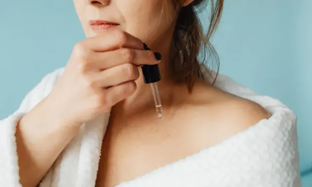 Une femme applique un sérum à base de peptide sur sa peau, enveloppée dans un peignoir blanc douillet.
