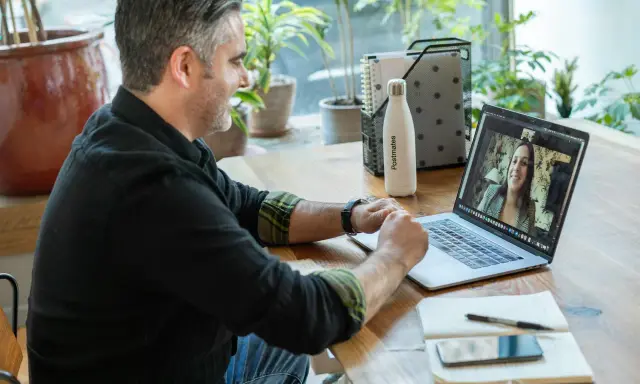 Mann gibt online Nachhilfe. Er lächelt und spricht mit einer Frau auf seinem Laptop.