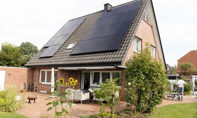 Tak på ett tegelhus med solceller som ger hög verkningsgrad. Solrosor blommar på uteplatsen.