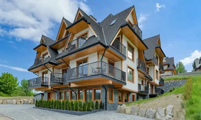 Nowoczesne apartamenty Bachledzki Wierch z drewnianymi elementami i balkonami, otoczone zielenią.
