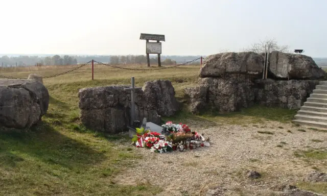 Pomnik na Górze Strękowej z krzyżem i wieńcami. W tle widoczne bunkry i krajobraz.