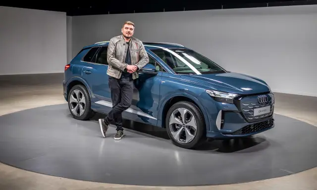 Ein Mann lehnt lässig an einem blauen Audi Q4 e-tron 2026.