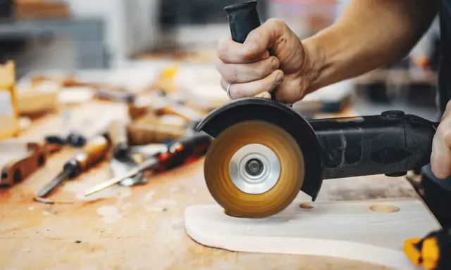 Mano trabajando con amoladora, mostrando sus usos en carpintería para dar forma a la madera.