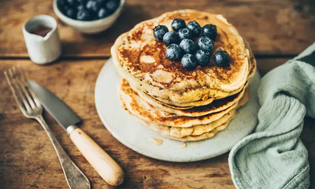 Pile de pancakes au levain garnis de myrtilles, sur une assiette, avec une fourchette et un couteau.