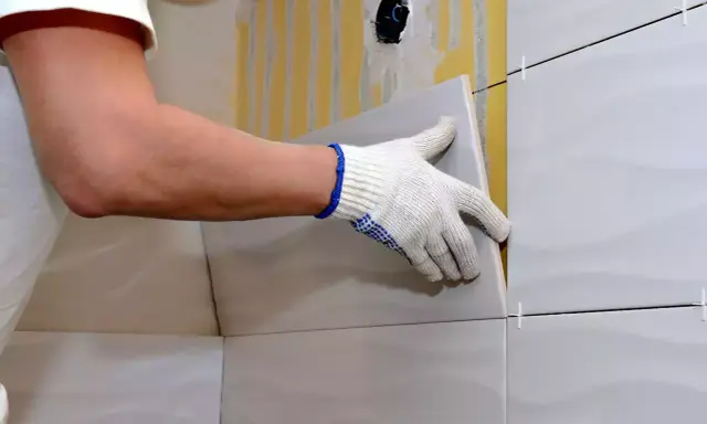 Man con guantes coloca una baldosa nueva sobre un alicatado existente.