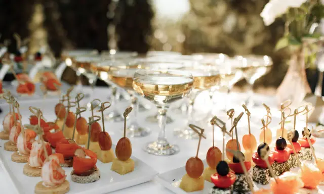 Elegantes aperitivos para bodas: camarones, salmón, queso y frutas en brochetas, junto a copas de champán.