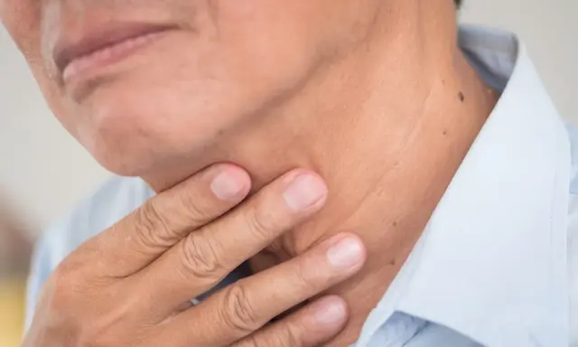 Dłoń dotyka szyi, gdzie znajdują się struny głosowe. Człowiek ma dwie struny głosowe.