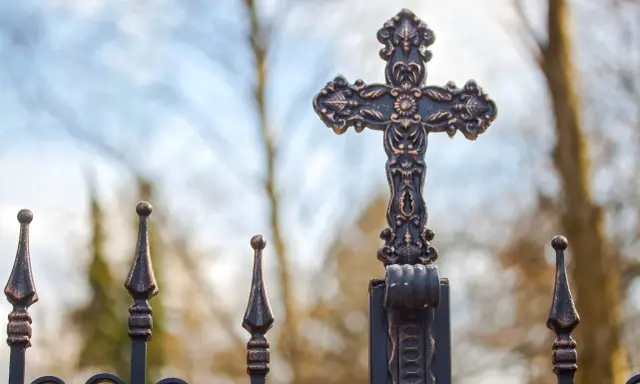 Krzyż na metalowym ogrodzeniu, symbol nadziei i walki z siedmioma grzechami głównymi.