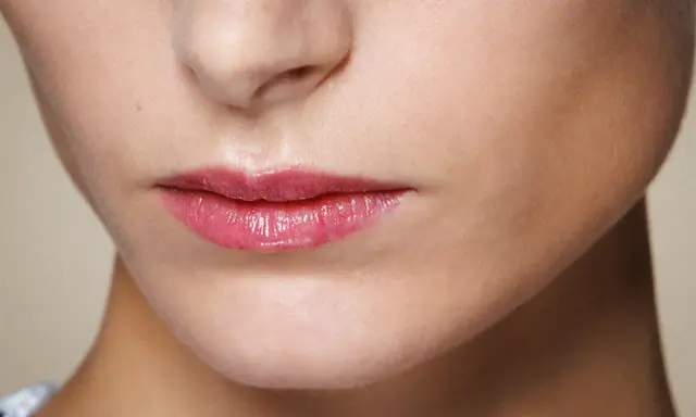 Labbra sottili e lucide con un tocco di gloss rosa, che catturano la luce.