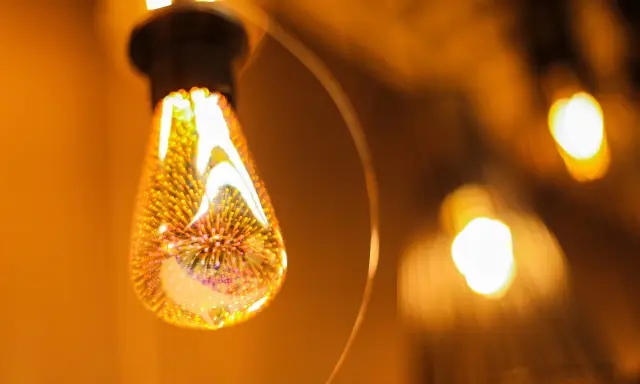 Une ampoule décorative aux filaments lumineux, projetant une lumière chaude et dorée. L'étiquette ampoule est subtilement intégrée dans le design.