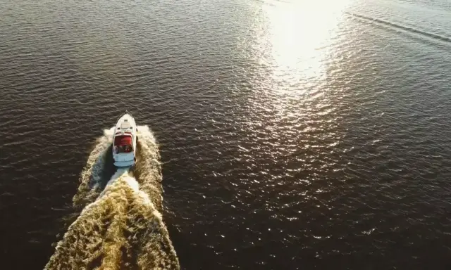 Bateau blanc naviguant sur l'eau sombre, laissant une traînée écumeuse. Le soleil brille, rappelant le temps de séchage Sikaflex.