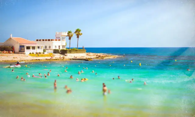 Sonnige Küste in Costa Calida, Spanien, mit vielen Menschen, die im türkisfarbenen Meer schwimmen.