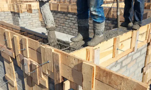 Vertiendo hormigón en el encofrado de construcción. Obreros con botas embarradas supervisan el proceso.