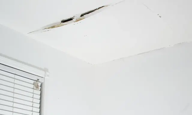 Widoczne pęknięcia na łączeniu sufitu i ściany, świadczące o problemach z konstrukcją lub wilgocią.