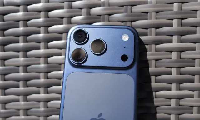 Niebieski iPhone 11 z potrójnym aparatem z tyłu, leżący na plecionej powierzchni.