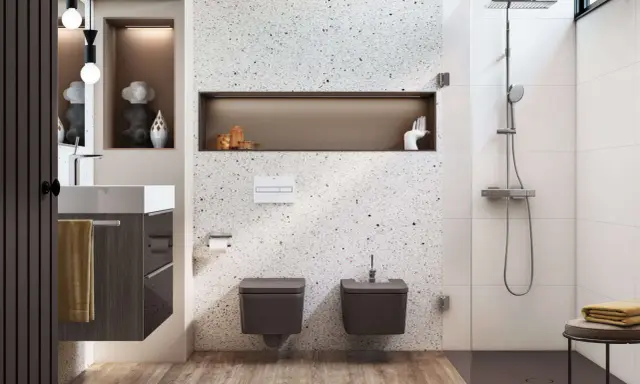Nowoczesna, wąska łazienka z prysznicem. W centrum uwagę przyciąga ściana z terazzo, a obok niej wiszące toalety i bidet.
