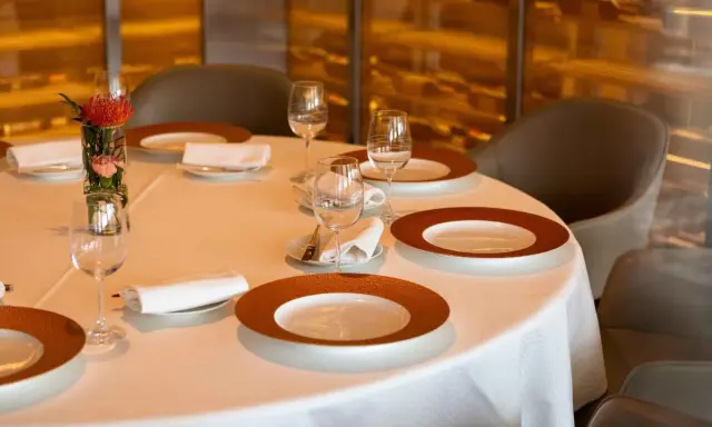 Une table dressée avec soin, des assiettes élégantes et des verres à moitié pleins, le tout dans une ambiance feutrée. L'art de la table est à l'honneur.